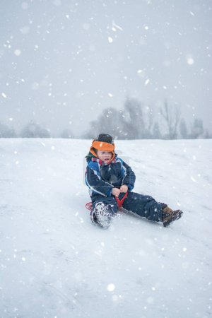 Téléchargez les photos : Petit garçon appréciant la randonnée en traîneau pendant les chutes de neige - en image libre de droit