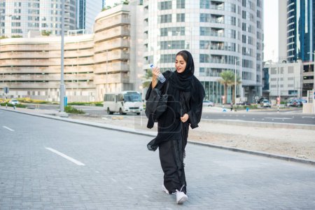 Photo for Beautiful Arab woman in abaya with water bottle and sports bag going to a gym - Royalty Free Image