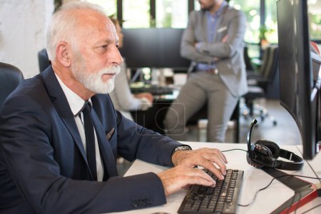 Téléchargez les photos : Homme d'affaires senior en vêtements de formalité travaillant sur ordinateur au bureau. - en image libre de droit
