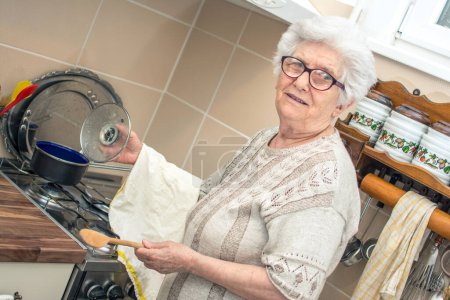 Téléchargez les photos : Souriant femme âgée cuisine dans la cuisine. - en image libre de droit