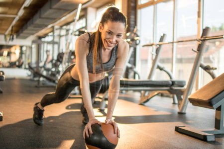 Téléchargez les photos : Ajustez jeune femme exerçant avec le ballon de médecine à la salle de gym. Fille sportive faisant de l'exercice de planche à l'aide de balle de fitness. - en image libre de droit