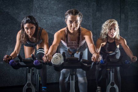 Photo for Group of young sporty women riding cycling bikes during spinning class indoors. - Royalty Free Image