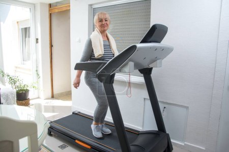 Photo for Active senior woman in sportswear using treadmill at home. Coronavirus Covid19 social distance. Home workout, active seniors, stay at home concept. - Royalty Free Image
