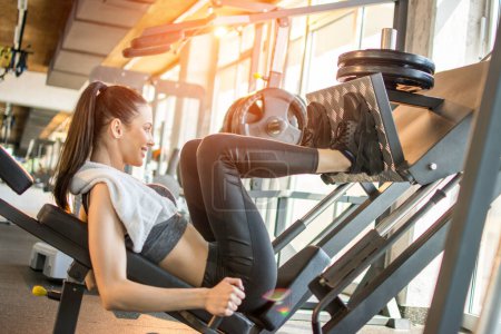 Photo for Side view of fit young sportswoman flexing her legs muscles on exercise machine at the gym during morning workout. - Royalty Free Image