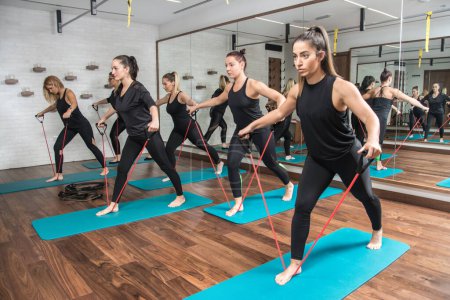 Téléchargez les photos : Groupe de filles sportives faisant de l'exercice avec un groupe de résistance dans un studio de fitness - en image libre de droit