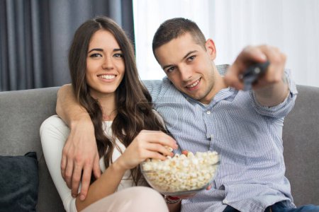 Téléchargez les photos : Jeune couple regarder la télévision et manger du pop-corn à la maison
. - en image libre de droit