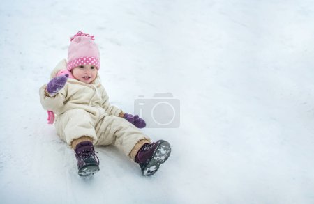 Téléchargez les photos : Petite fille mignonne qui s'amuse pendant la descente de la colline par temps neigeux - en image libre de droit