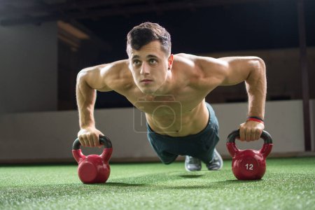 Foto de Hombre musculoso sin camisa haciendo flexiones con campanas de caldera en el gimnasio. - Imagen libre de derechos