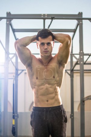 Foto de Retrato de un joven guapo sin camisa sujetando la correa y mirando a la cámara en el gimnasio. - Imagen libre de derechos
