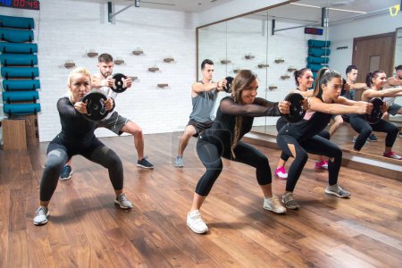 Foto de Mujeres y hombres deportistas haciendo ejercicio junto con pesas en el club de salud. - Imagen libre de derechos