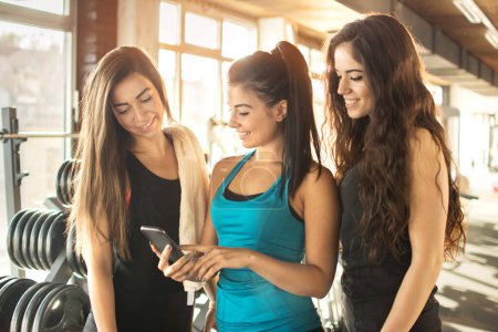 Gruppe sportlicher Freundinnen nutzt Smartphone im Fitnessstudio.