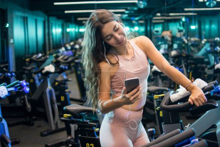 Foto de Joven mujer deportiva escuchando música con auriculares en el estudio de ciclismo - Imagen libre de derechos