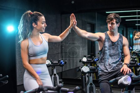 Photo for Fitness woman and man giving each other a high five after cycling training in gym. Fit couple high five after workout in health club. - Royalty Free Image