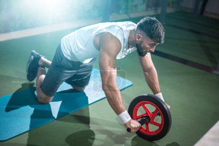 Foto de Deportista muscular haciendo ejercicio con rueda de fitness en el gimnasio. - Imagen libre de derechos