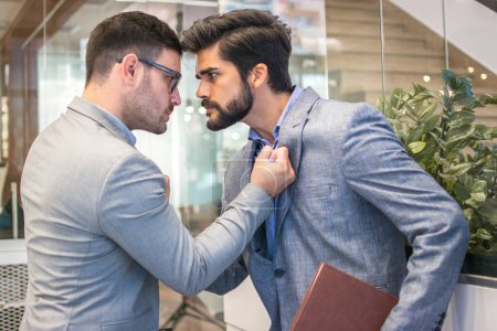 Geschäftskonflikt zwischen zwei Geschäftsleuten in formeller Kleidung im Büro. Chef und Mitarbeiter mit aggressivem Gesichtsausdruck bekämpfen sich.