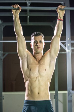 Foto de Retrato del hombre musculoso haciendo entrenamiento de fuerza en barra horizontal en el gimnasio. - Imagen libre de derechos