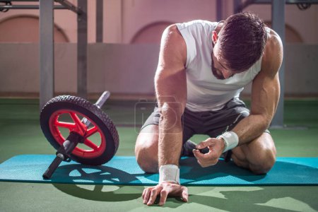 Foto de Hombre musculoso agotado tomando un descanso de hacer ejercicio con rueda de ab en el gimnasio. - Imagen libre de derechos