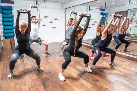 Photo for Group of sporty young women and men exercising together with weights in health club. - Royalty Free Image