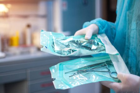 Nahaufnahme von Zahnarzthänden in weißen sterilen Handschuhen, die zahnärztliche Werkzeuge für chirurgische Zwecke in einer Schutzfolie in der Zahnarztpraxis verpackt halten