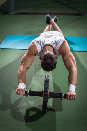 Above view of muscular man doing exercises with ab wheel at gym.