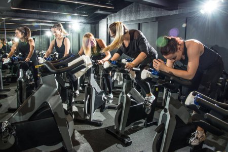 Téléchargez les photos : Groupe de femmes sportives utilisant des vélos d'exercice pour l'entraînement dans la salle de gym - en image libre de droit