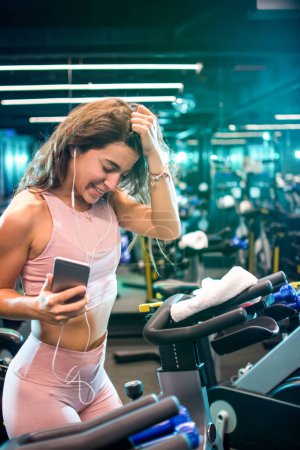Foto de Chica alegre y deportiva escuchando música con auriculares en un gimnasio - Imagen libre de derechos