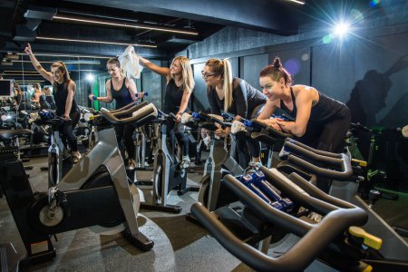 Photo for Group of cheerful sporty girls working out on exercise bikes and having fun together on cycling class at gym. - Royalty Free Image