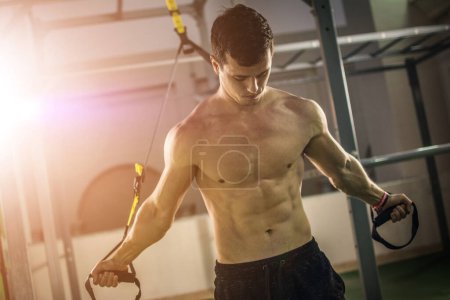 Foto de Muscular hombre sin camisa de entrenamiento con correas de fitness en el gimnasio. - Imagen libre de derechos