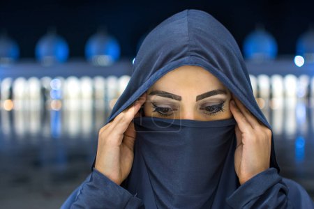 Téléchargez les photos : Gros plan portrait de belle jeune femme musulmane portant le hijab regardant vers le bas près de la mosquée la nuit. - en image libre de droit