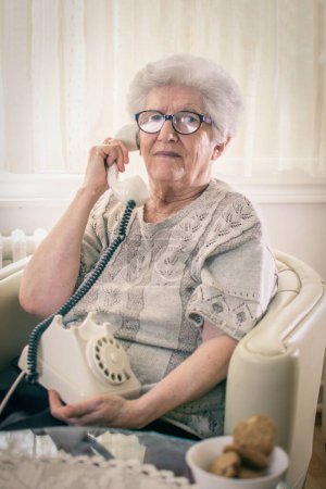 Téléchargez les photos : Femme âgée parlant au téléphone fixe à la maison. - en image libre de droit