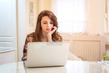 Photo for Young woman working with laptop computer at home, serious, thinking - Royalty Free Image