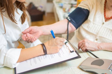 Ärztin schreibt Blutdruckwerte an Klemmbrett einer Seniorin