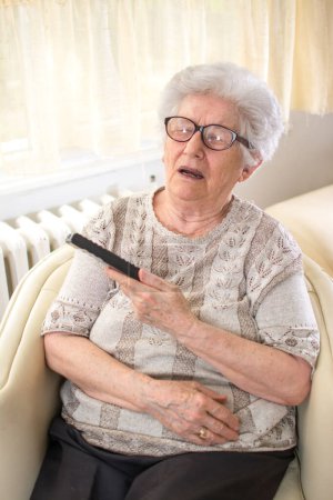 Téléchargez les photos : Femme âgée avec télécommande s'est endormie sur un fauteuil après avoir regardé la télévision. - en image libre de droit