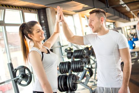 Téléchargez les photos : Couple sportif se donnant cinq après une séance d'entraînement réussie dans la salle de gym - en image libre de droit