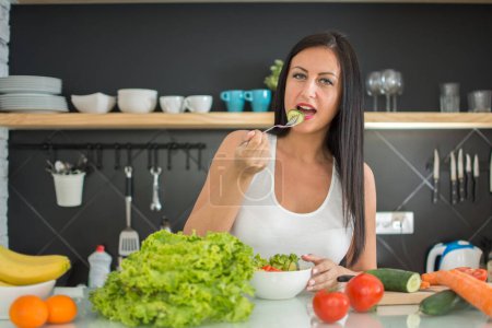Photo for Young woman eating fresh salad in the kitchen - Royalty Free Image