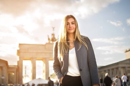 Téléchargez les photos : Portrait d'une jeune femme souriante et à la mode devant Brandenburger Tor à Berlin, Allemagne - en image libre de droit