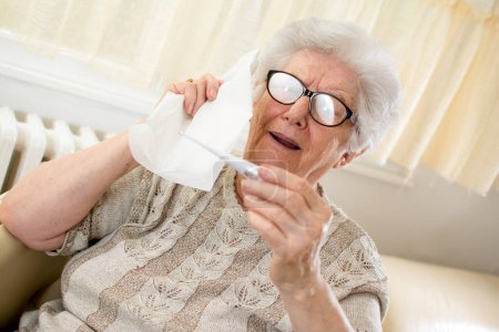 Foto de Mujer mayor comprobando la temperatura corporal con termómetro y sujeción - Imagen libre de derechos