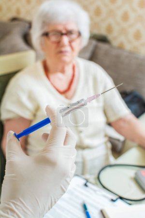 Photo for Close up of hand holding injection. Senior patient in the background - Royalty Free Image