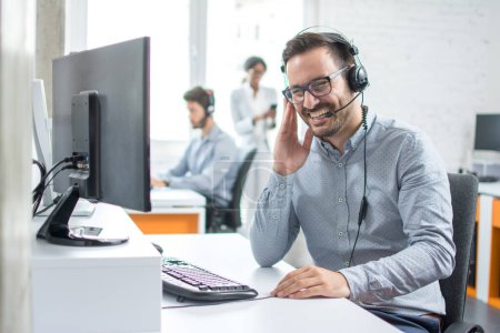 Téléchargez les photos : Répartiteur de soutien technique joyeux parlant avec le client en utilisant un casque dans le centre d'appel. - en image libre de droit