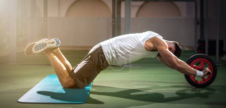 Foto de Vista panorámica del hombre guapo haciendo ejercicio con rueda de fitness en la azotea, gimnasio al aire libre. - Imagen libre de derechos