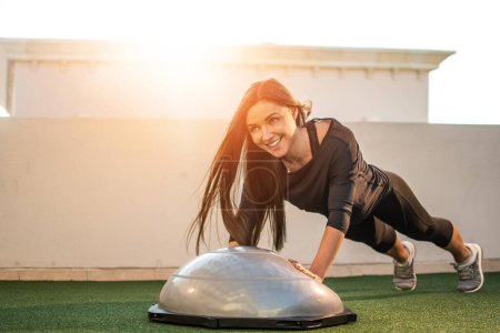 Photo for Beautiful smiling fit girl doing push ups on half-ball outdoors. - Royalty Free Image