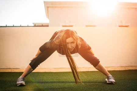 Photo for Fit girl in sportswear exercising at rooftop outdoors during sunset. - Royalty Free Image