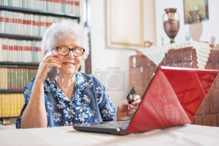 Foto de Compras en línea, edad y concepto de tecnología. Mujer mayor cerca del ordenador portátil con tarjeta de crédito y teléfono inteligente - Imagen libre de derechos