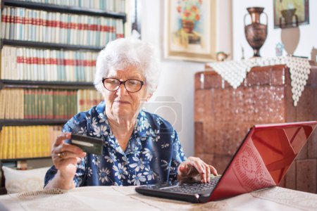 Photo for Old woman looking at credit card and typing its data to online form - Royalty Free Image