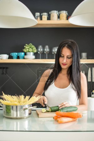 Foto de Mujer joven cortando pepino fresco en la tabla de cortar en la cocina - Imagen libre de derechos