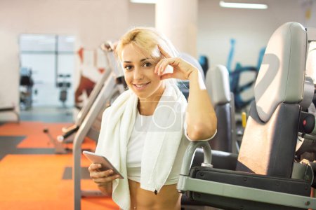 Photo for Young woman with towel and smartphone in a gym. - Royalty Free Image
