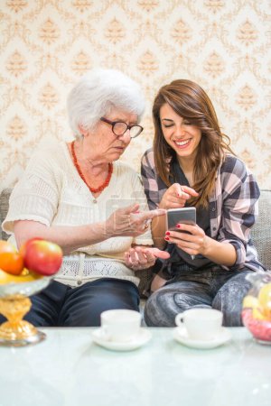Photo for Grandmother and granddaughter commenting social media feeds on smart phone - Royalty Free Image