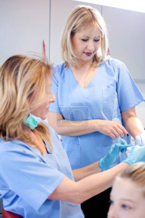 Foto de Odontóloga de mediana edad explicando modelo de dientes a enfermera en clínica dental - Imagen libre de derechos