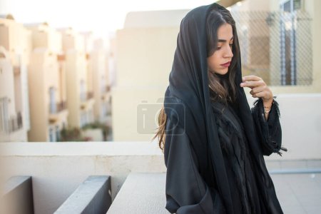 Foto de Hermosa mujer joven de Oriente Medio usando ropa árabe tradicional de pie y mirando hacia abajo al aire libre. - Imagen libre de derechos
