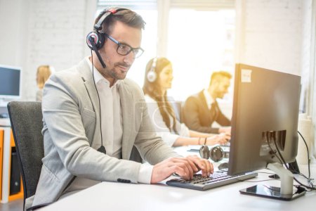 Photo for Male technical support service operator wearing headset working on desktop computer in office - Royalty Free Image